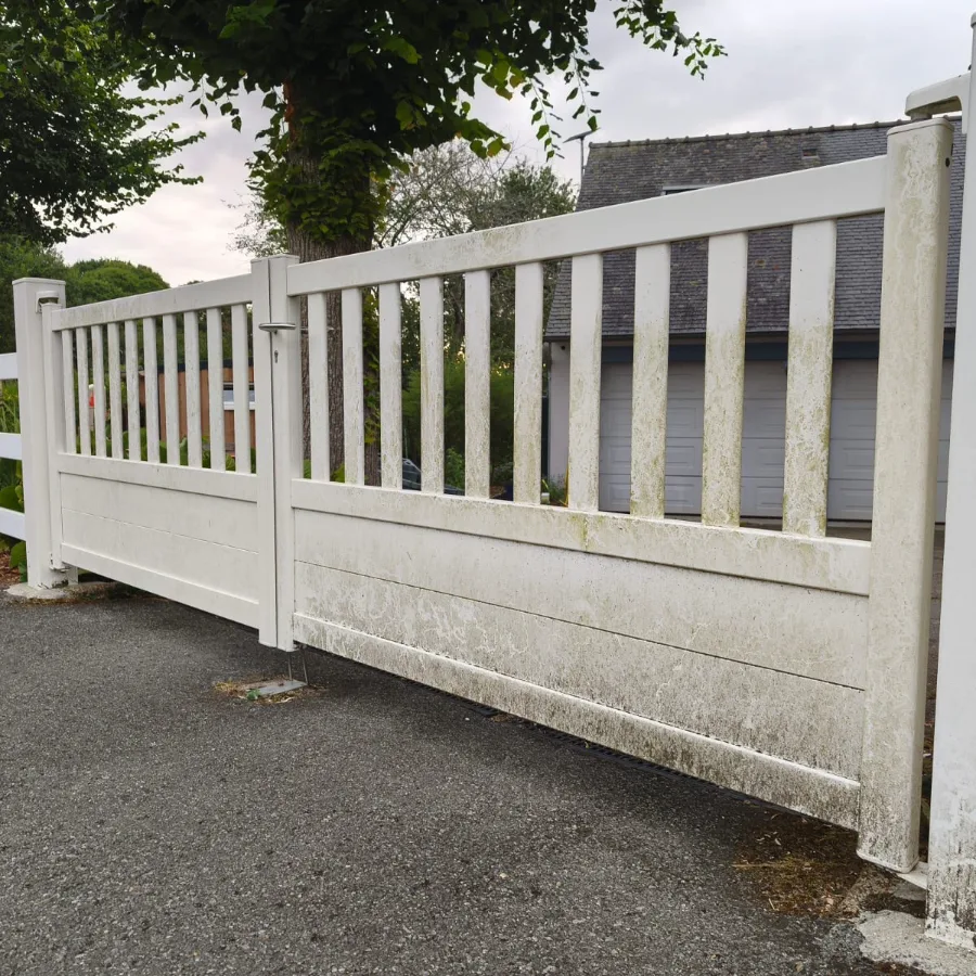 Portail coulissant en PVC blanc avant nettoyage : les panneaux et les barreaux sont striés de vert et de gris