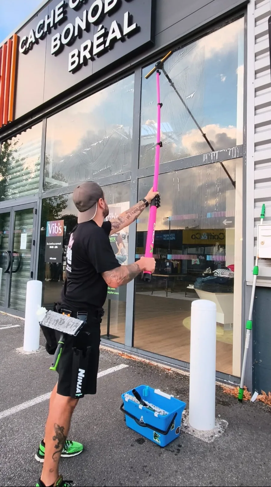 Jérôme lave à la perche télescopique le vitrage haut d'une devanture d'enseigne, sous le caisson lumineux du magasin