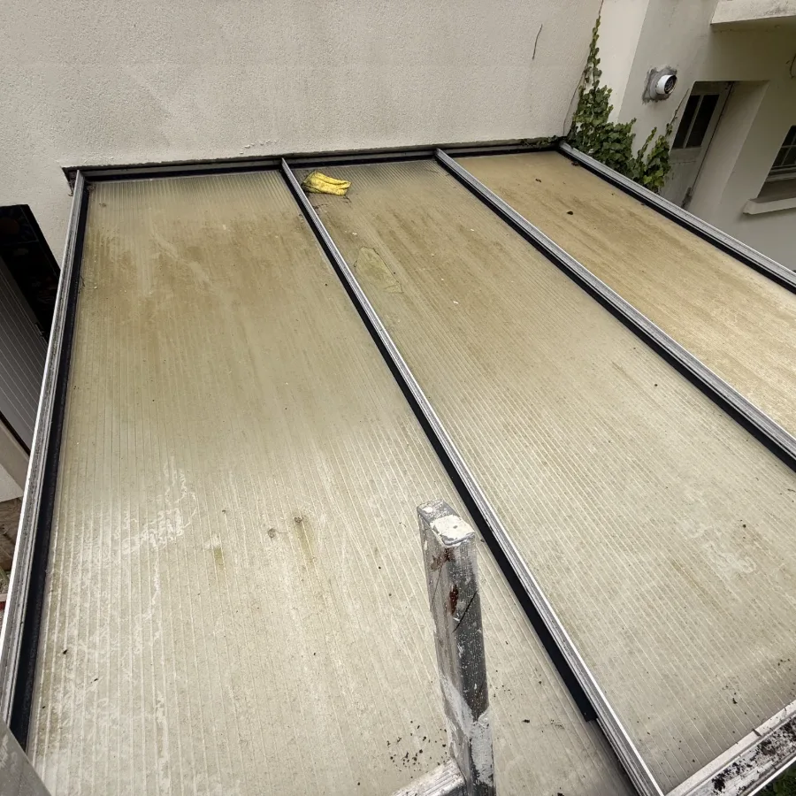 Toiture de véranda avant nettoyage : les plaques de polycarbonate sont couvertes d'un dépôt vert et jaune qui bloque la lumière