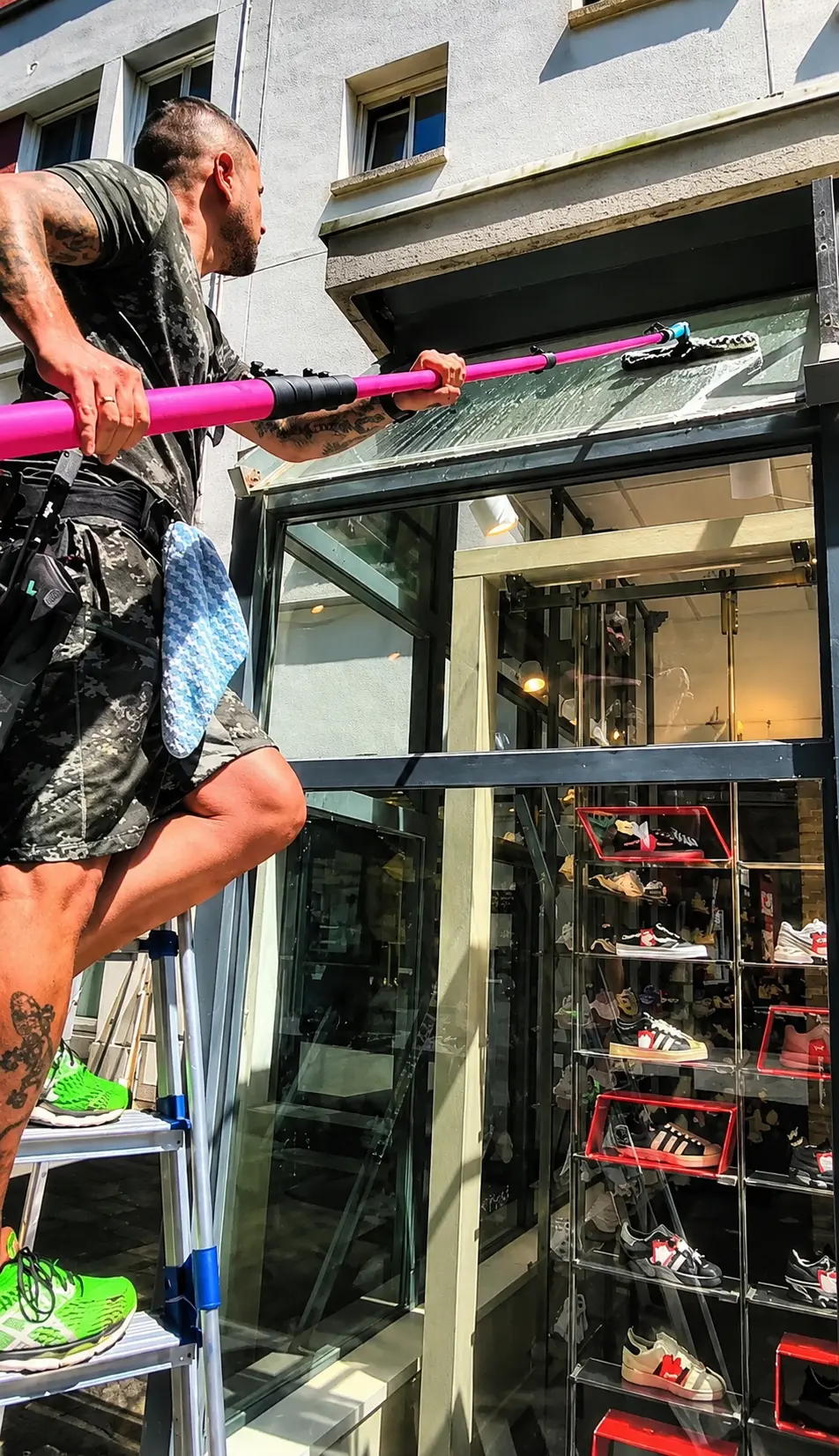Jérôme, de Many Clean, lave la vitrine d'un magasin de chaussures à la perche télescopique depuis un escabeau