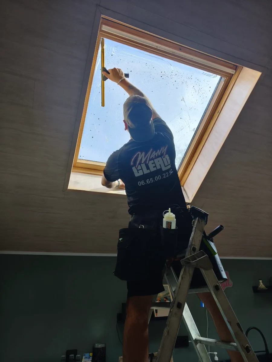Jérôme, de Many Clean, nettoie un Velux à la raclette depuis un escabeau, vu d'en dessous